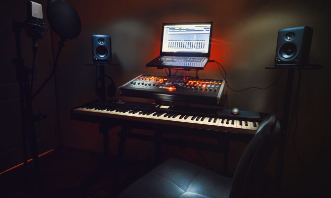 Interior of a small bedroom recording studio, details of equipment, microphone in foreground and modern mixing console with laptop in background.